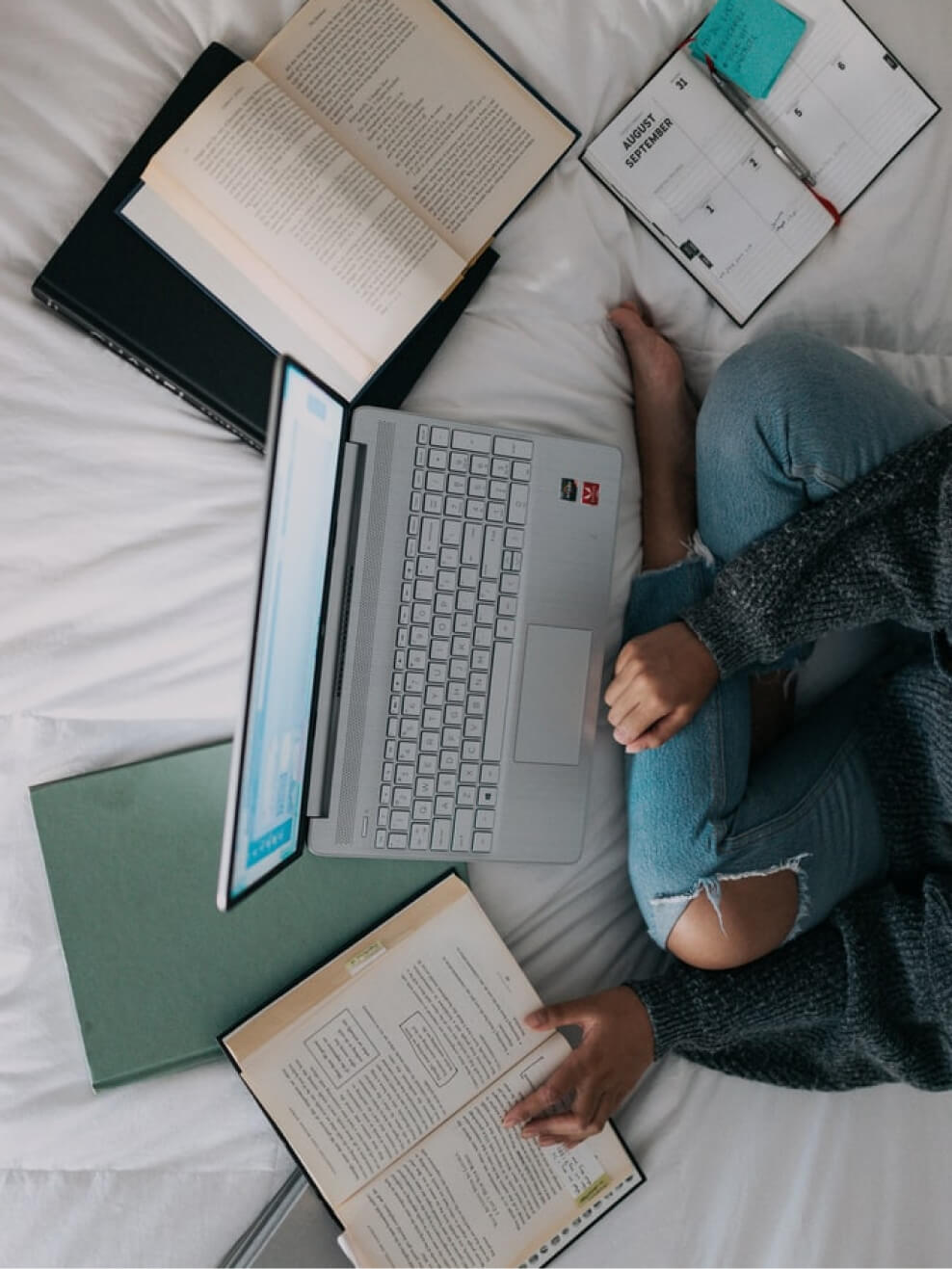woman with computer and book on bed